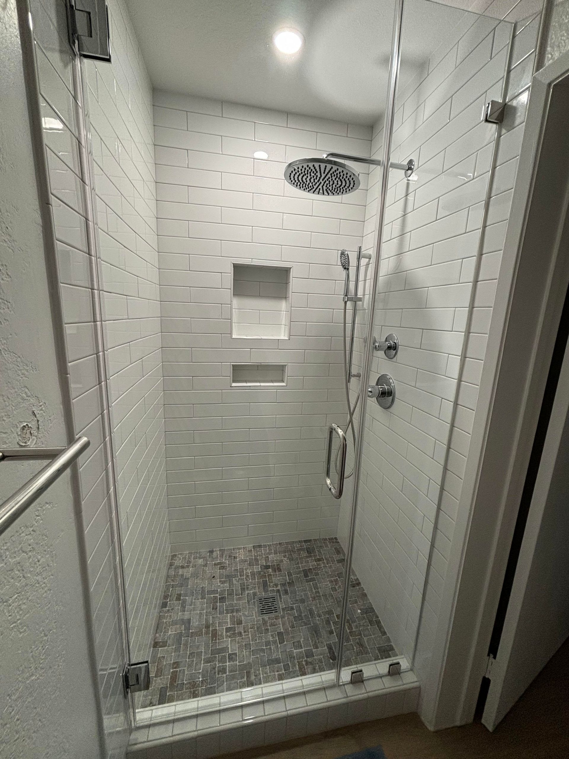A shower with a glass door and a shower head in a bathroom.