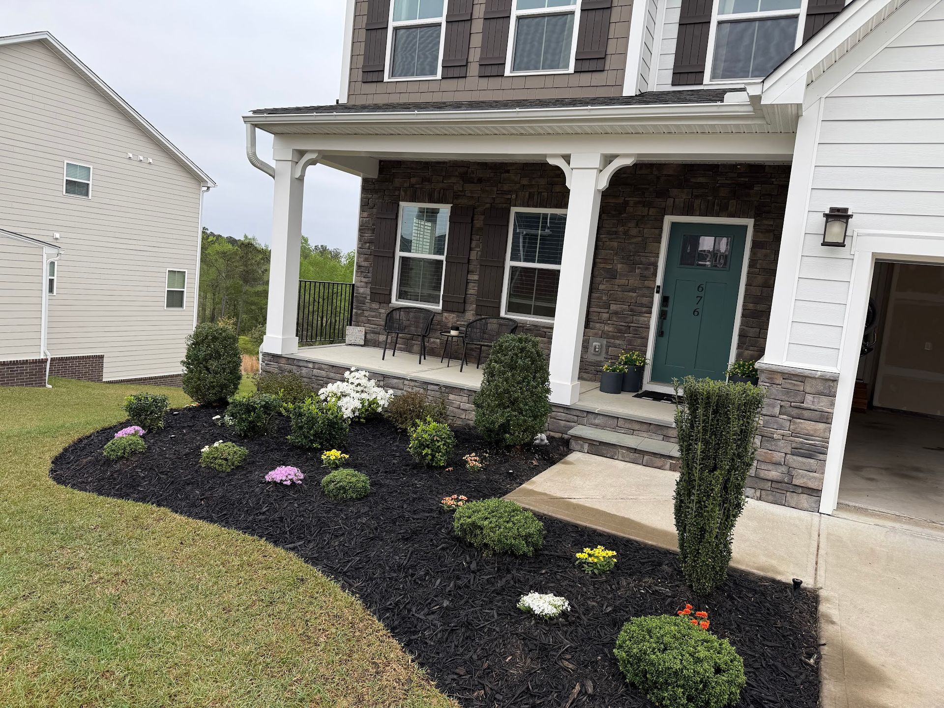 House with a porch and landscaped flowerbed with black mulch, green bushes and colorful flowers.