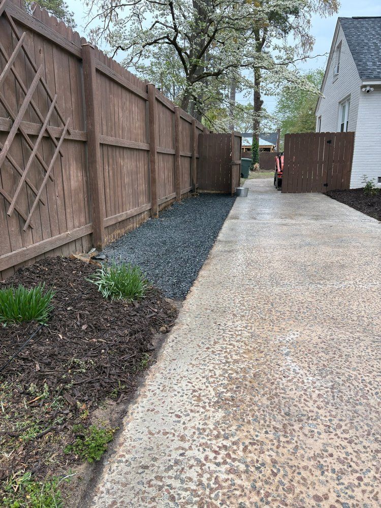 Long brown fence and driveway, with a gravel path alongside.