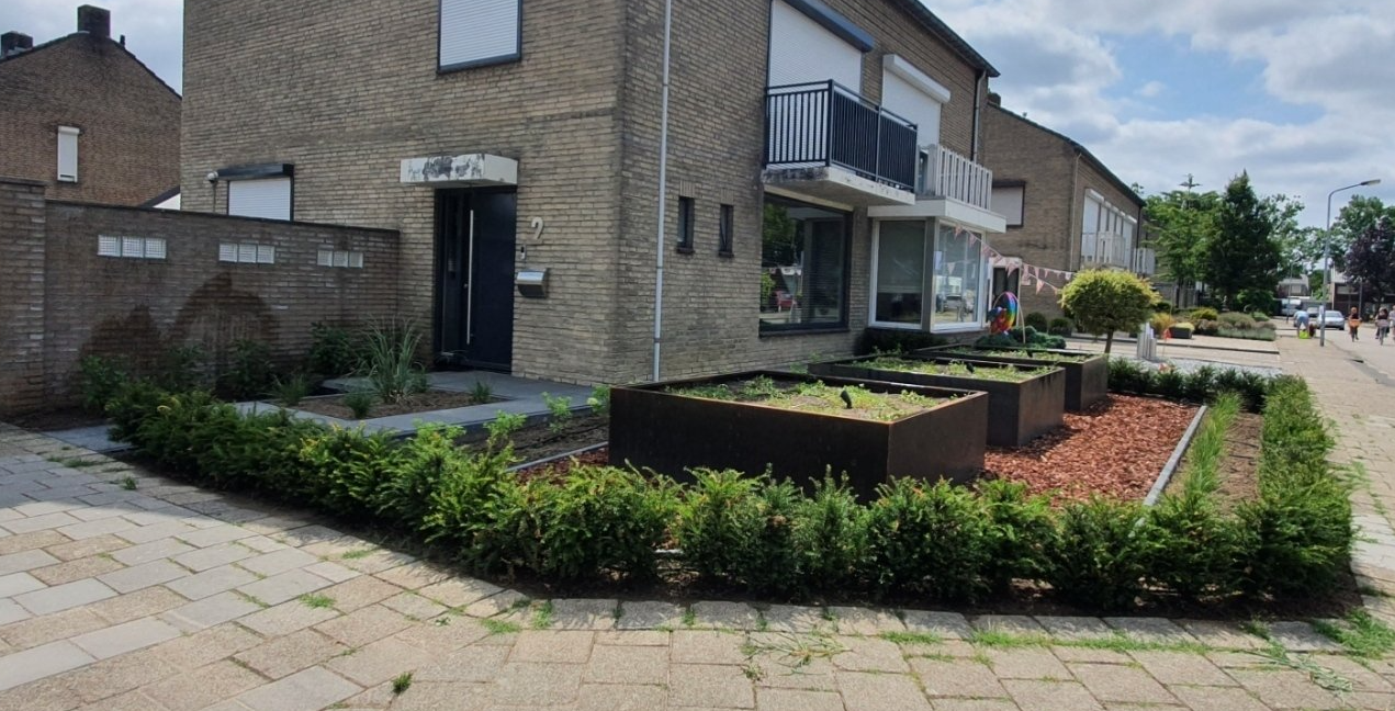 Moderne rijtjeshuizen met balkons, aangelegde voortuinen en een bestraat trottoir langs de straat.