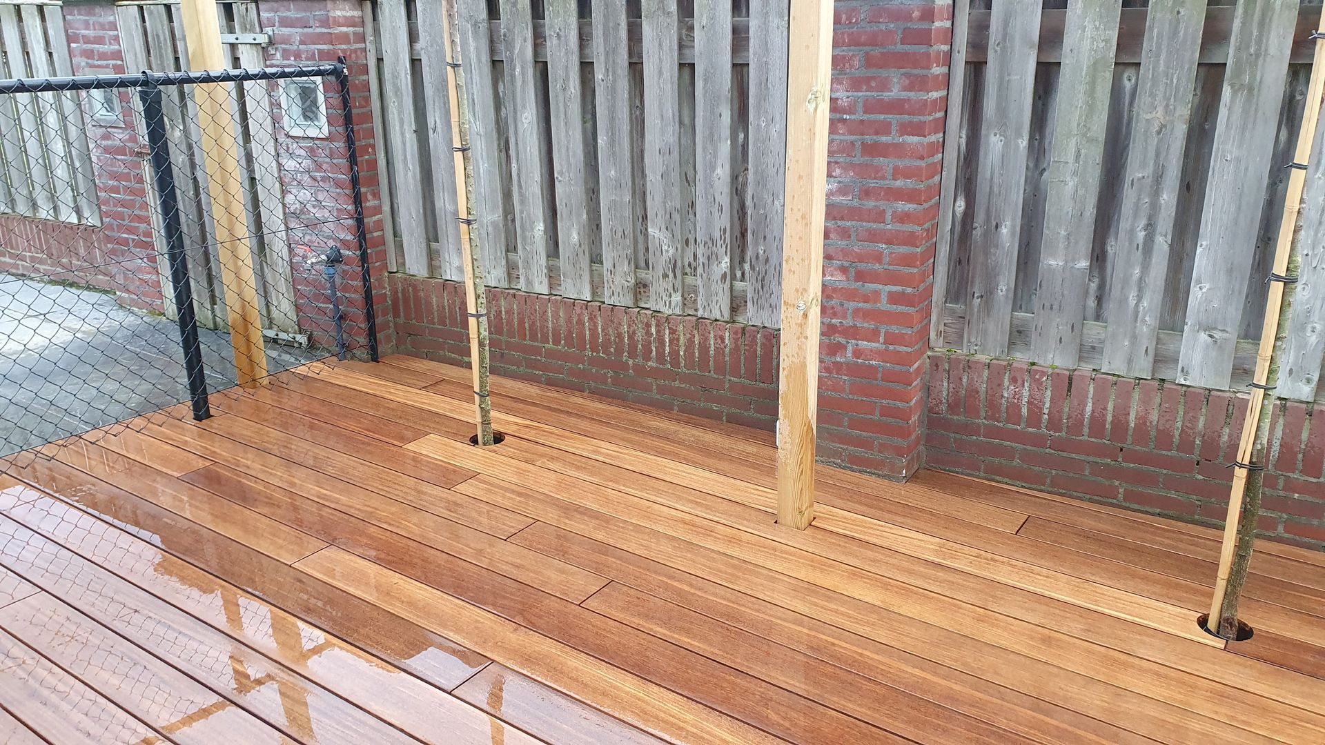 Houten terras met twee waslijnpalen naast een bakstenen muur en een houten schutting.