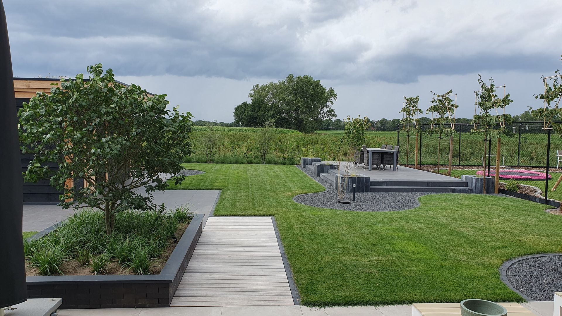 Moderne daktuin met groen gazon, bestraat pad, plantenbakken en een bewolkte hemel.