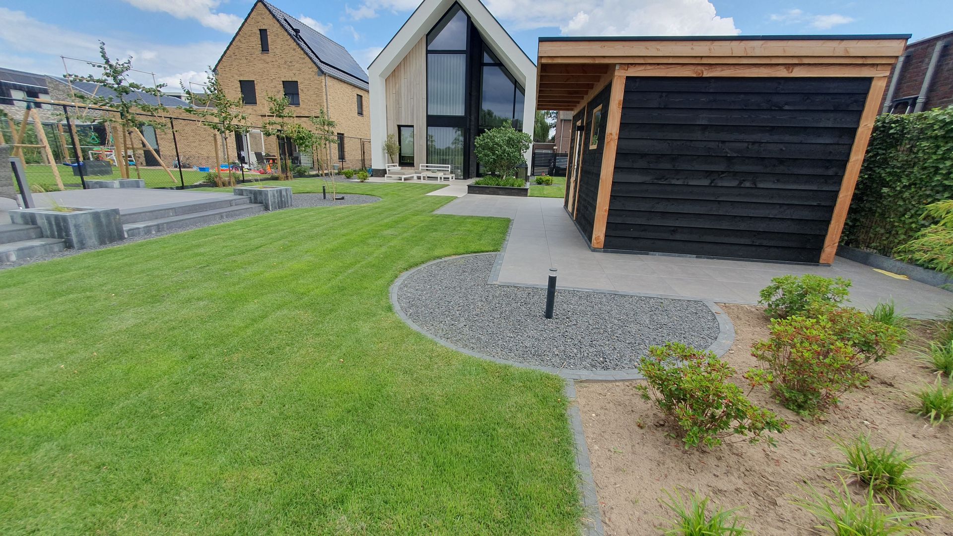 Moderne woning met een zwarte garage, groen gazon, grindoprit en een aangelegde voortuin.