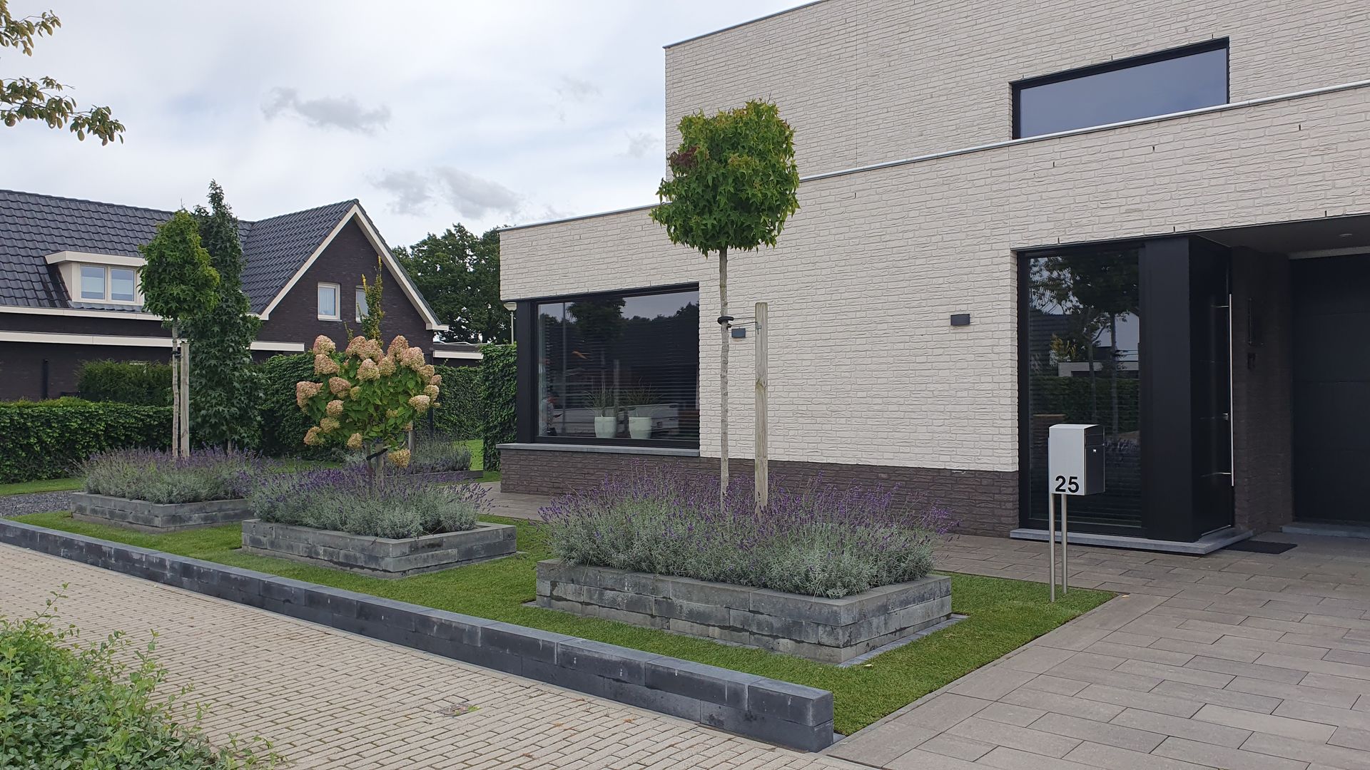 Moderne woning met grijze gevel en aangelegde voortuin langs een trottoir.