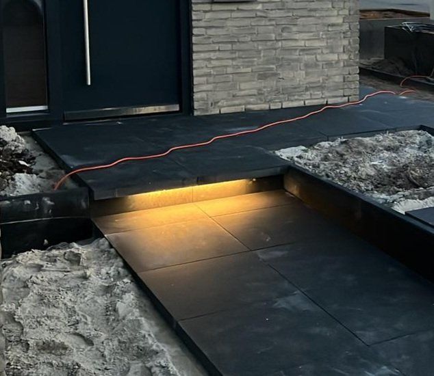 Moderne huisingang met verlichte traptreden, donker looppad en sneeuw aan beide zijden.