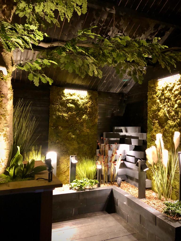 Binnentuin met vijver, waterval, weelderig groen en zachte sfeerverlichting.