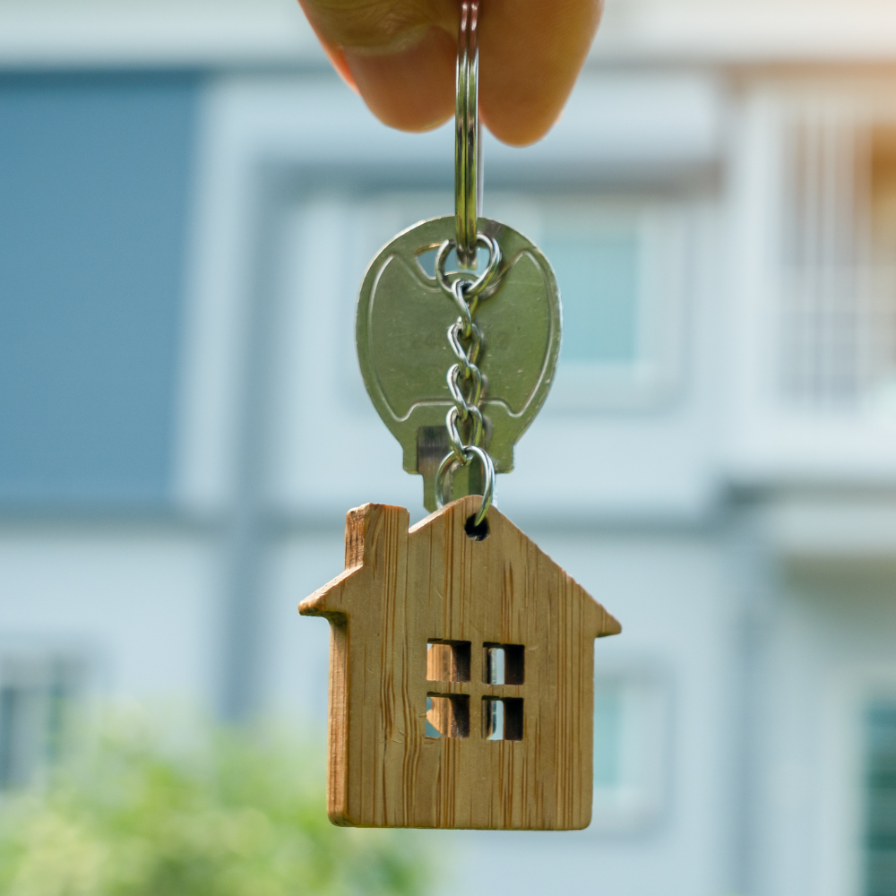 A person is holding a key with a house keychain attached to it.