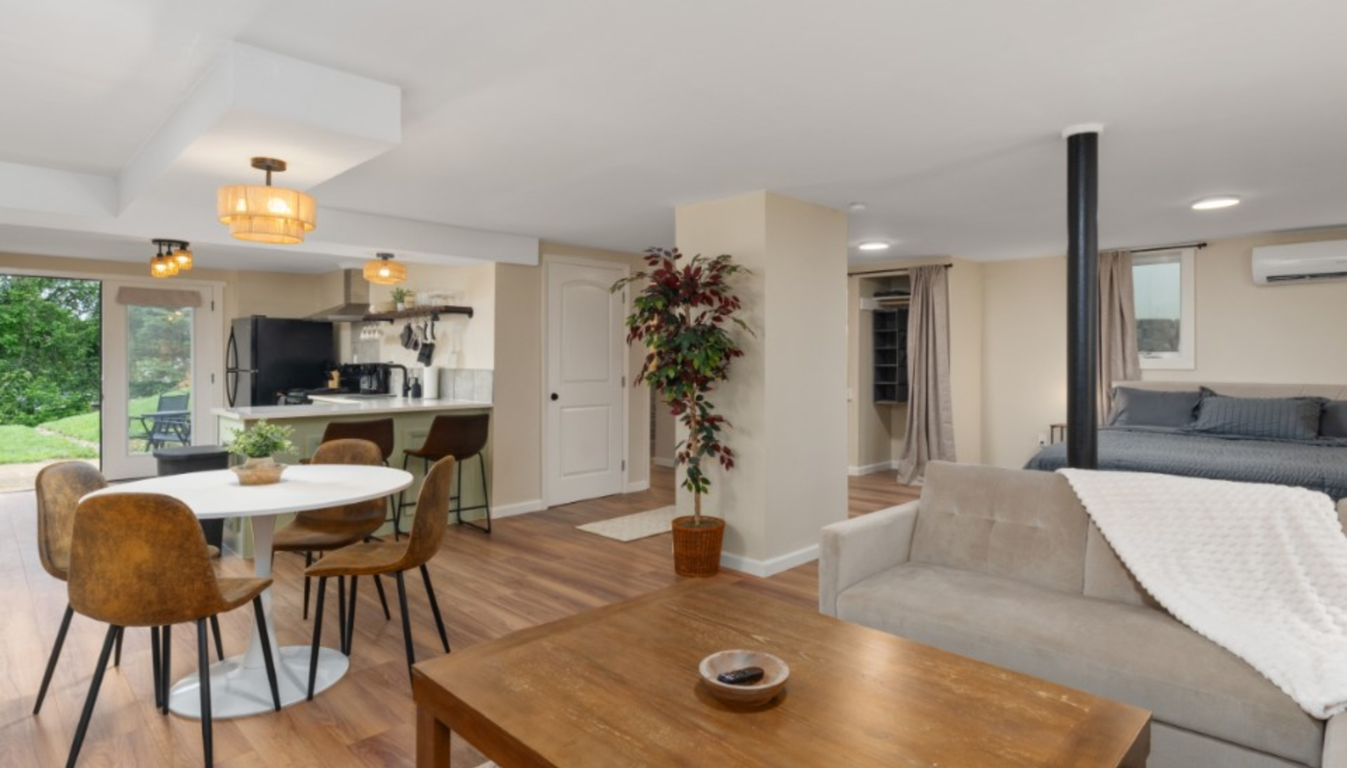 Open concept living space: living room with sofa, dining area, and kitchen with wood floors, earth tones.