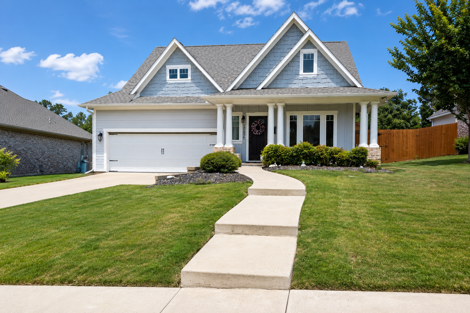 Suburban house with white trim, front porch, two-car garage, and a curved walkway under a blue sky