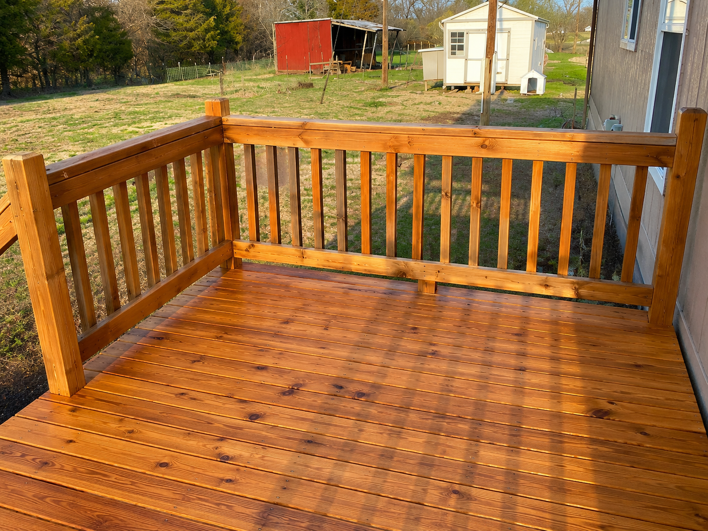 Wooden deck with railings overlooking a yard, with a shed and house in the background.