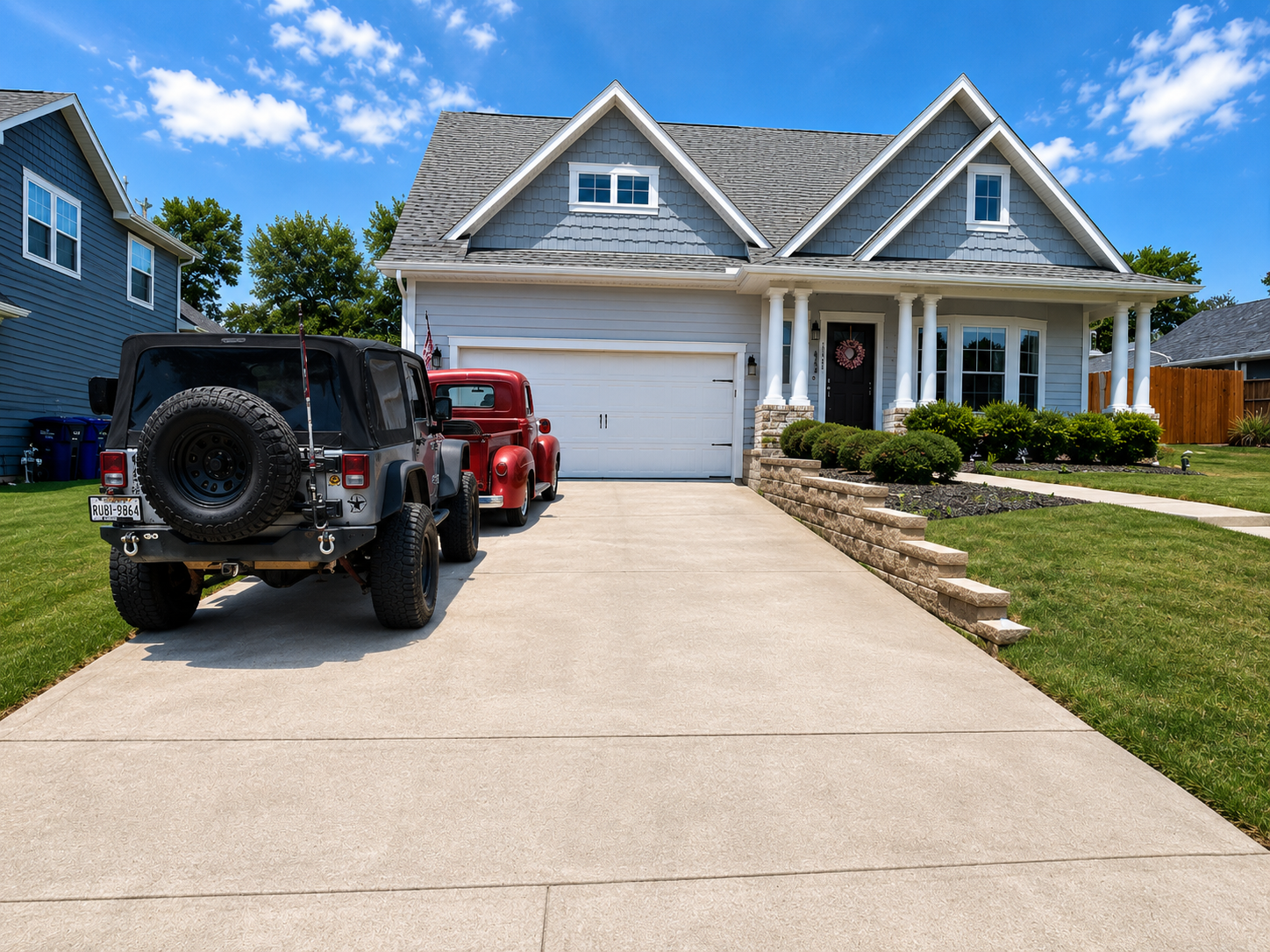 Blue suburban house with white trim, a red Jeep and black SUV in the driveway, and a manicured lawn