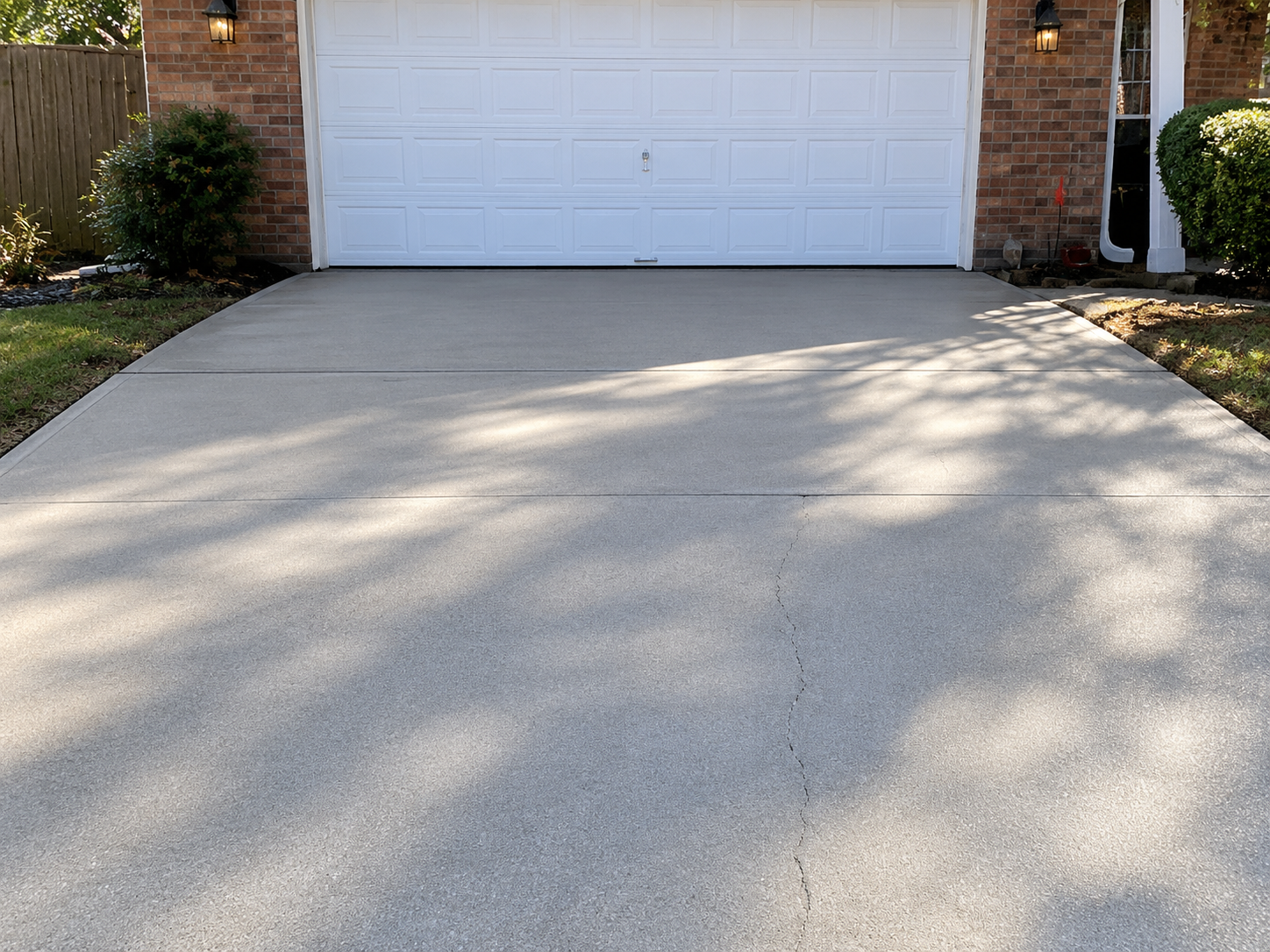 Concrete driveway leading to a white garage door with brick siding and shrubs on both sides