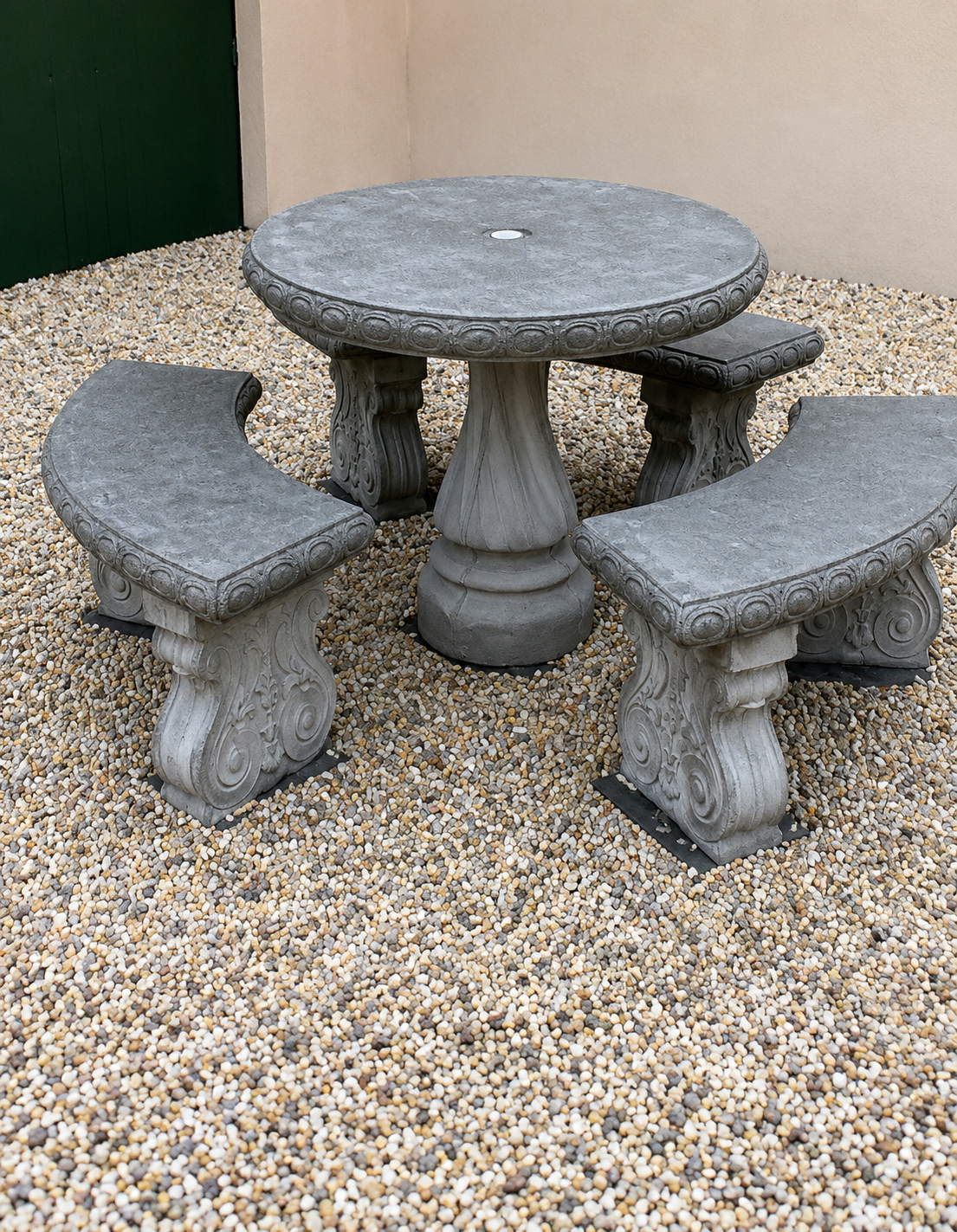 Stone patio table with three matching curved benches on gravel outdoors