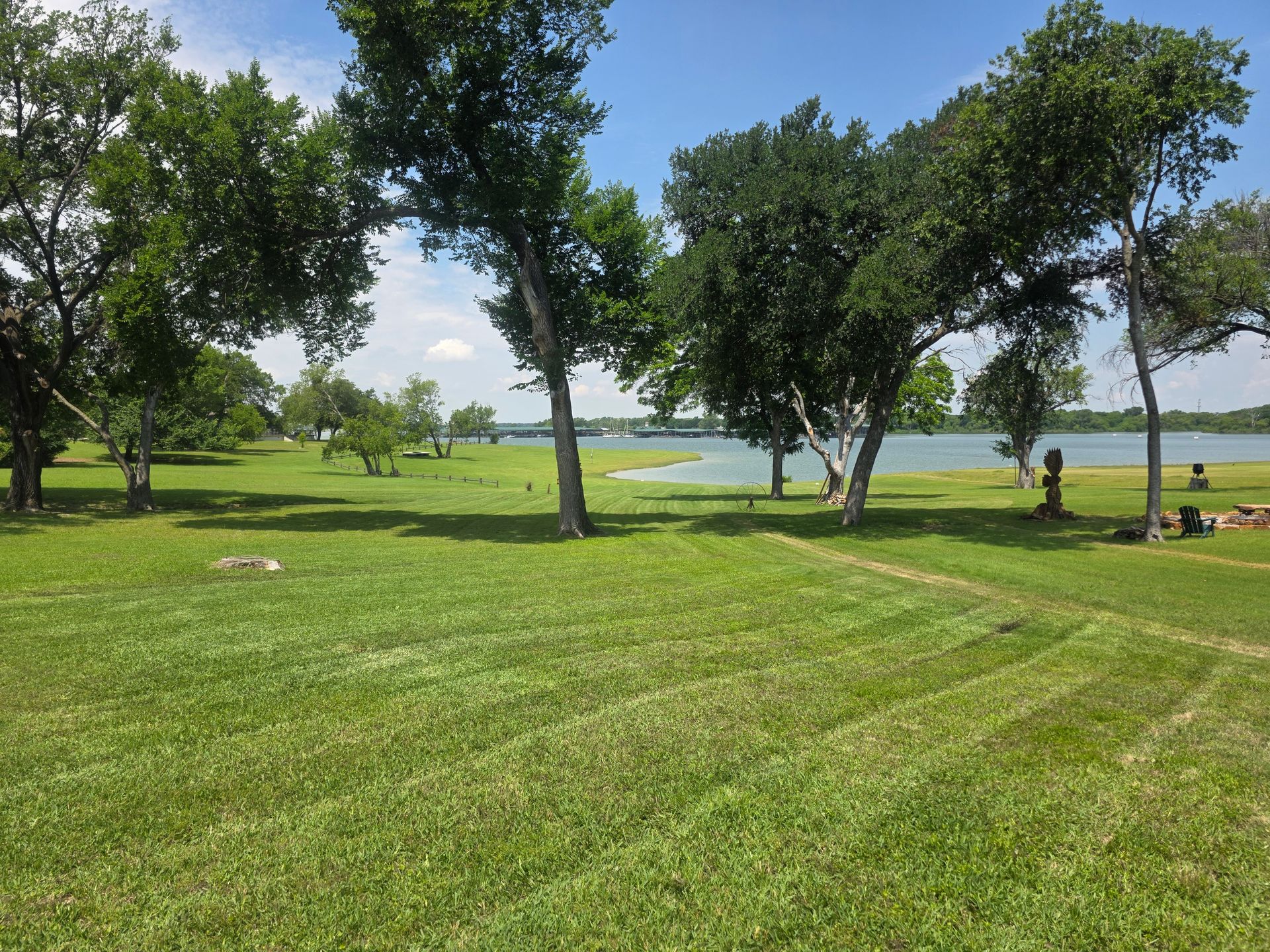 Grassy lakeside park with scattered trees and a few people near the water