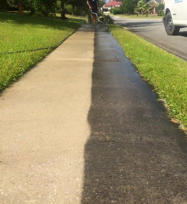 Damaged sidewalk with a dark repaired strip beside a grassy street edge and parked car