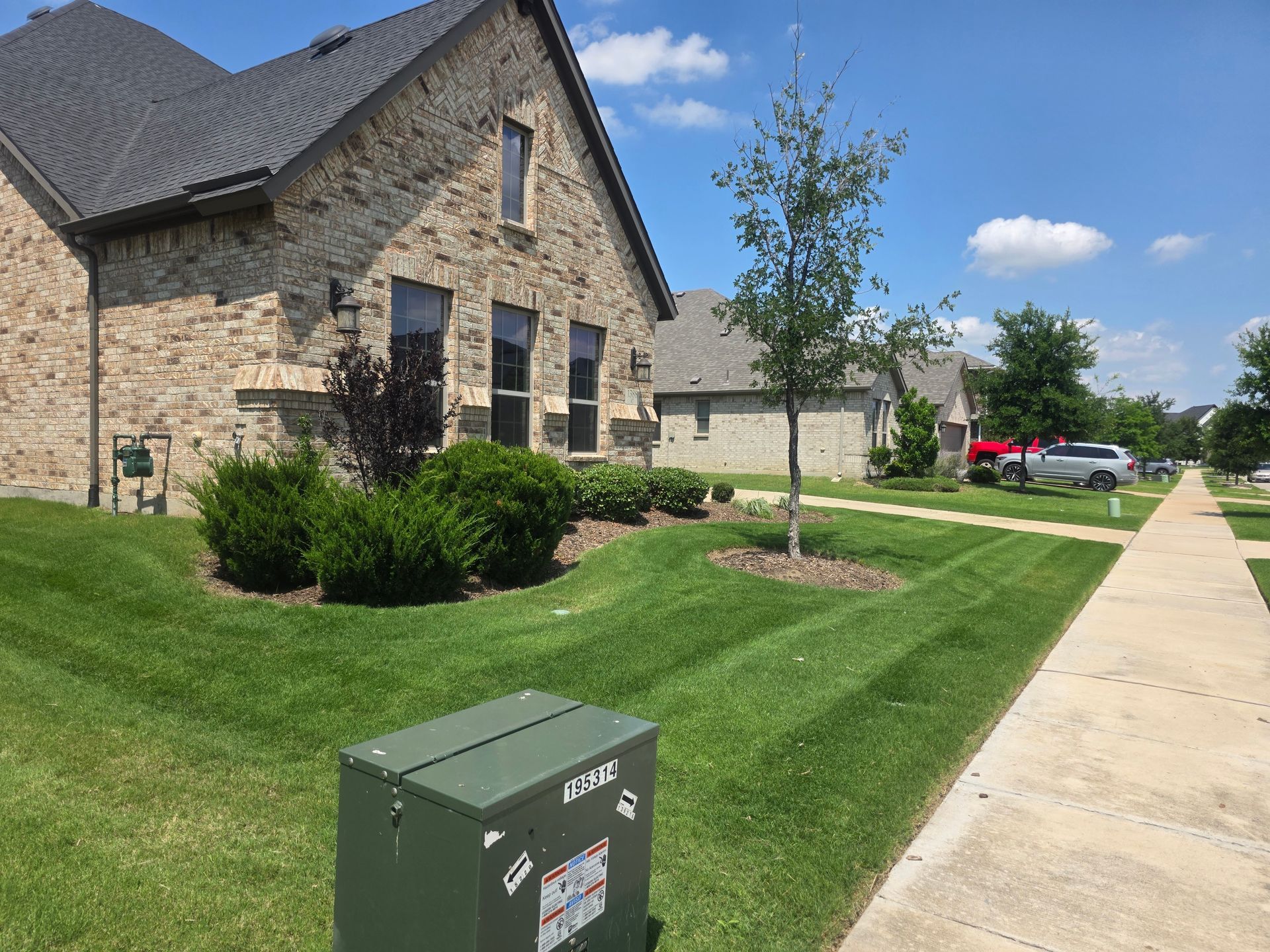 Stone apartment building beside a sidewalk and grassy lawn on a sunny day