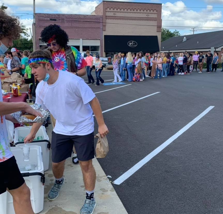 A man wearing a tie dye shirt is pouring water into a cooler