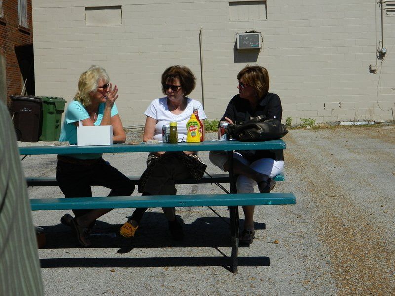 Three women sit at a picnic table with a bottle of mustard on it