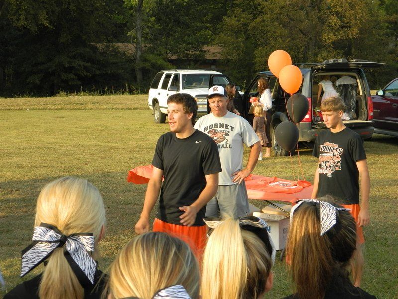 A man wearing a hornets shirt stands in front of a group of people
