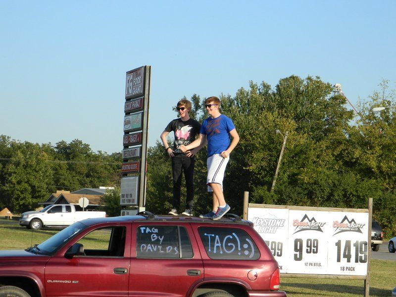 Two men standing on top of a red car that says tag on it