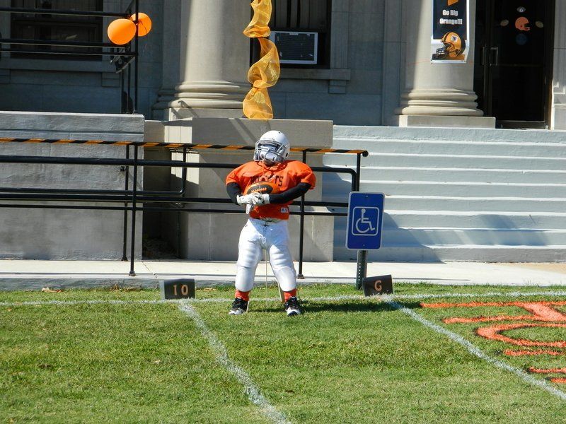 A young boy in an orange football uniform is standing on a field in front of a handicap sign