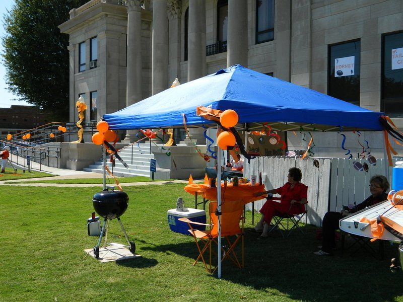 People sit under a blue tent in front of a building
