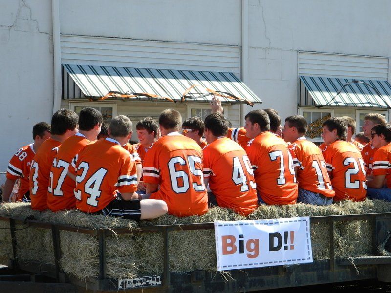 A group of young men in orange jerseys sit on a wagon with a sign that says big d