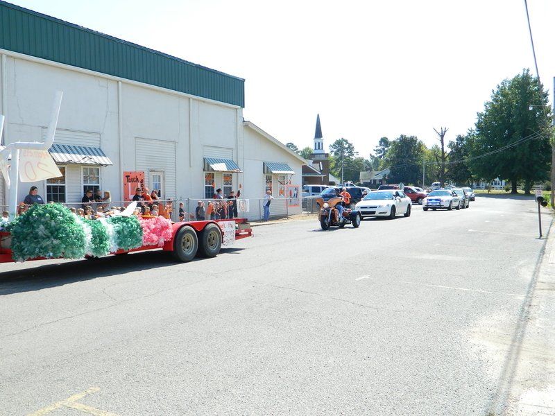 A row of cars are driving down a street in front of a building