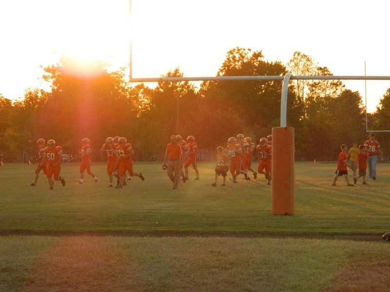 A group of football players are running on a field at sunset