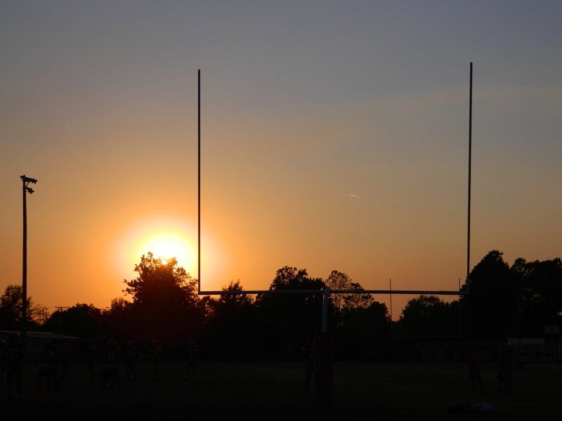 A sunset over a football field with a goal post in the foreground