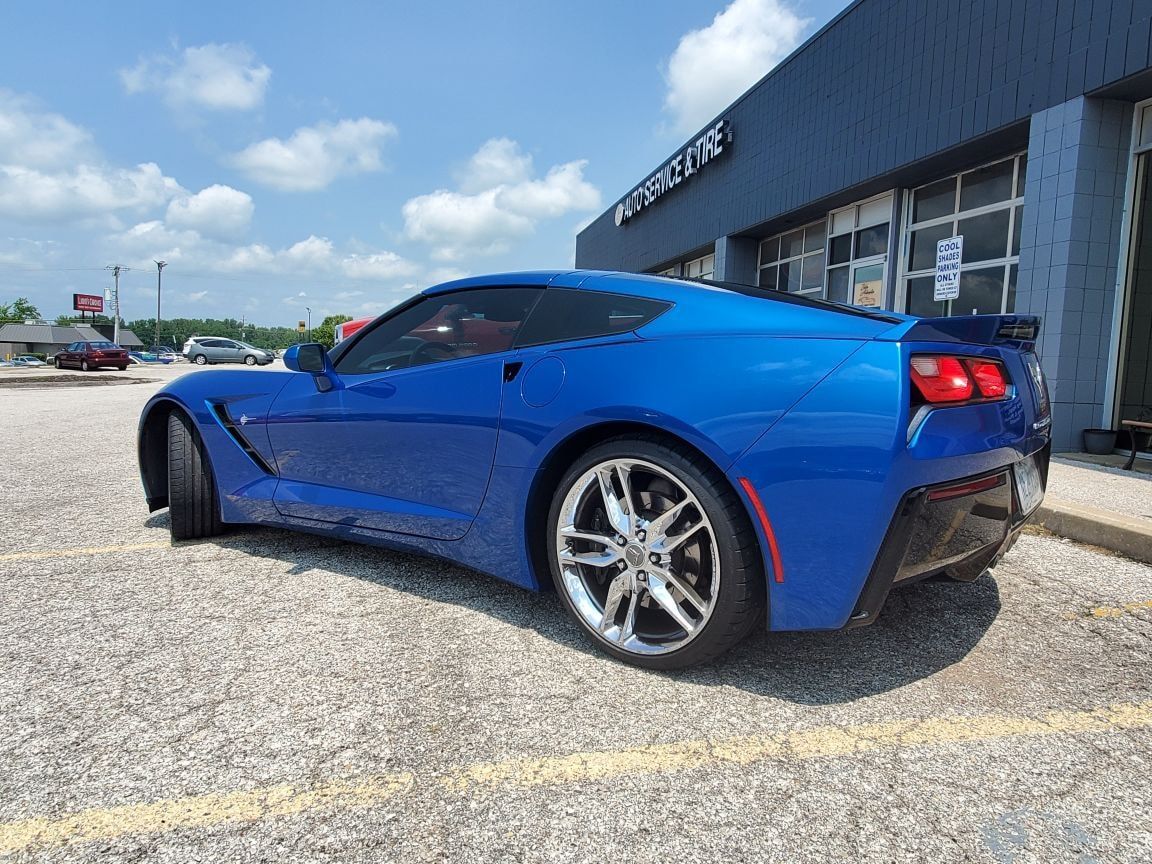 Blue sports car parked on gravel beside a building under a partly cloudy sky