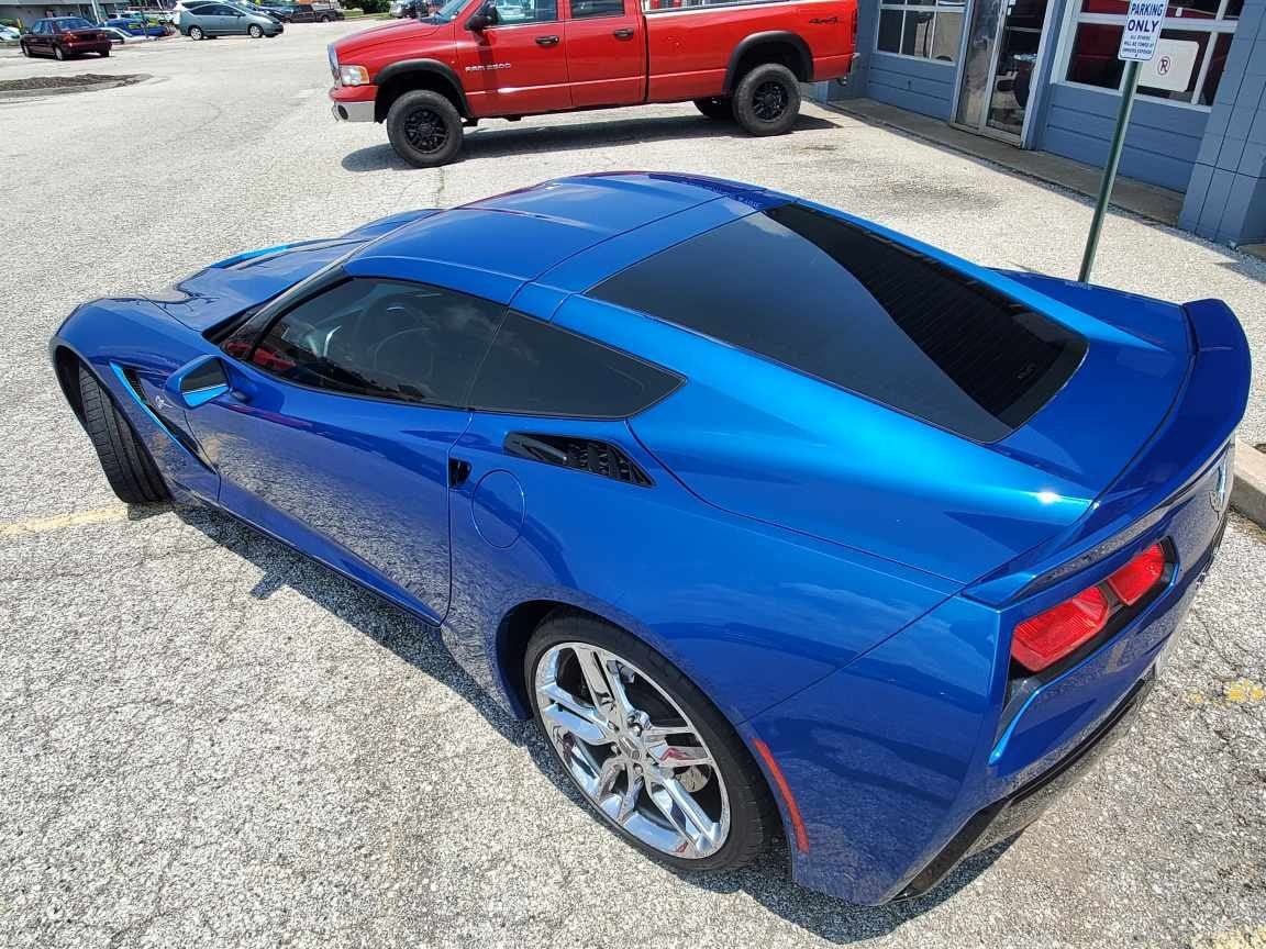 Blue sports coupe parked outside a building, seen from the rear quarter, with a red pickup in the background