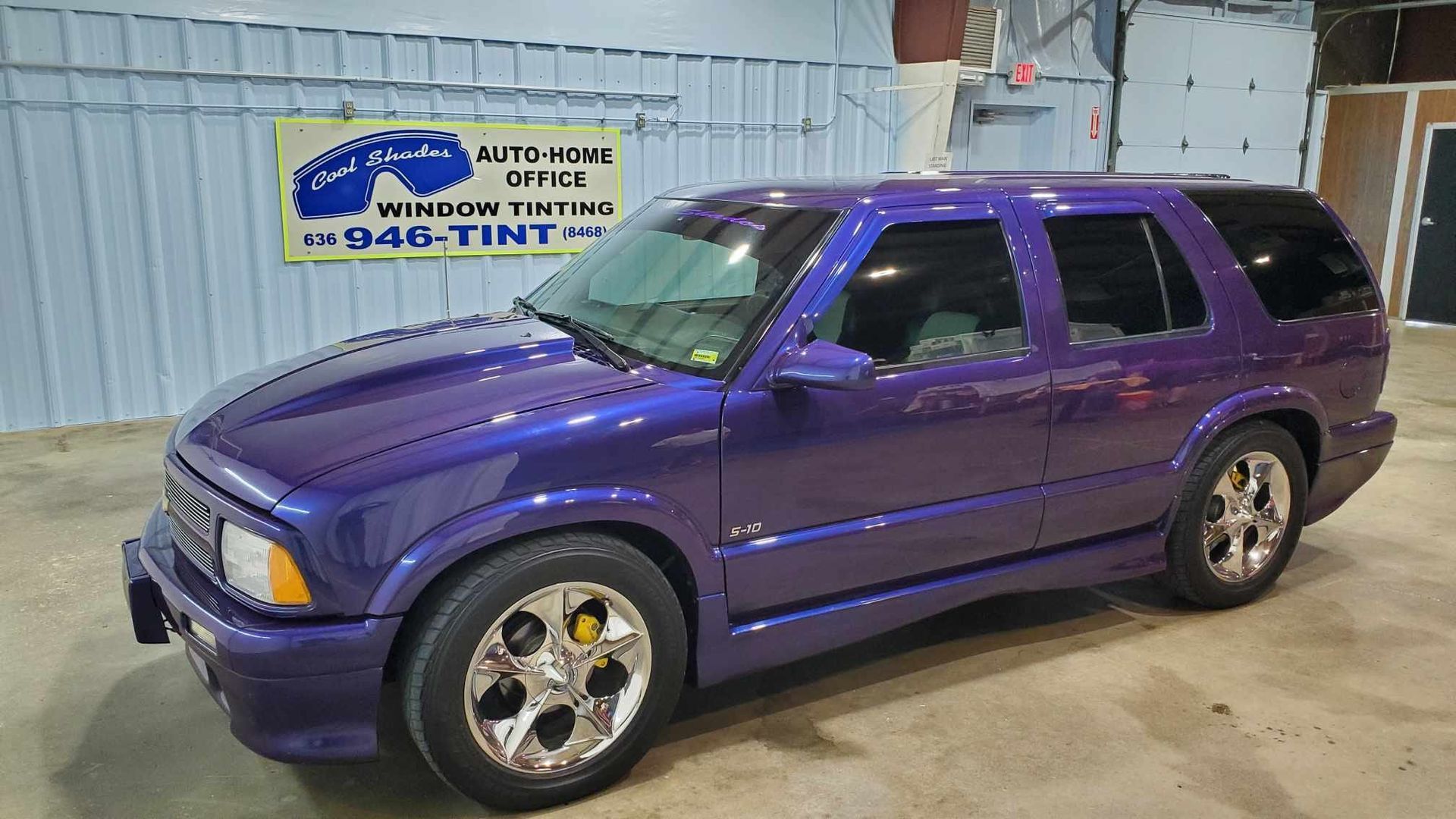 Purple SUV parked indoors next to a sign on a concrete floor