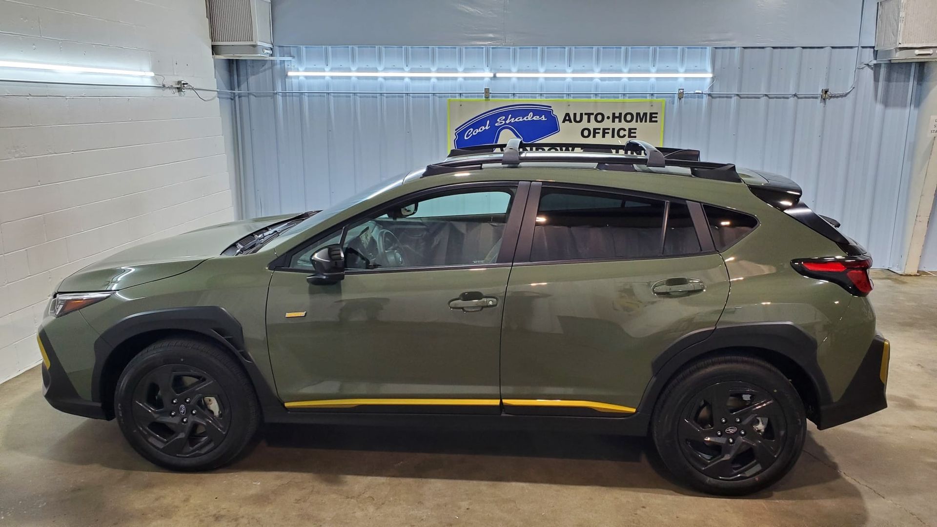 Green SUV parked indoors on a lift, side view with black wheels and yellow trim.