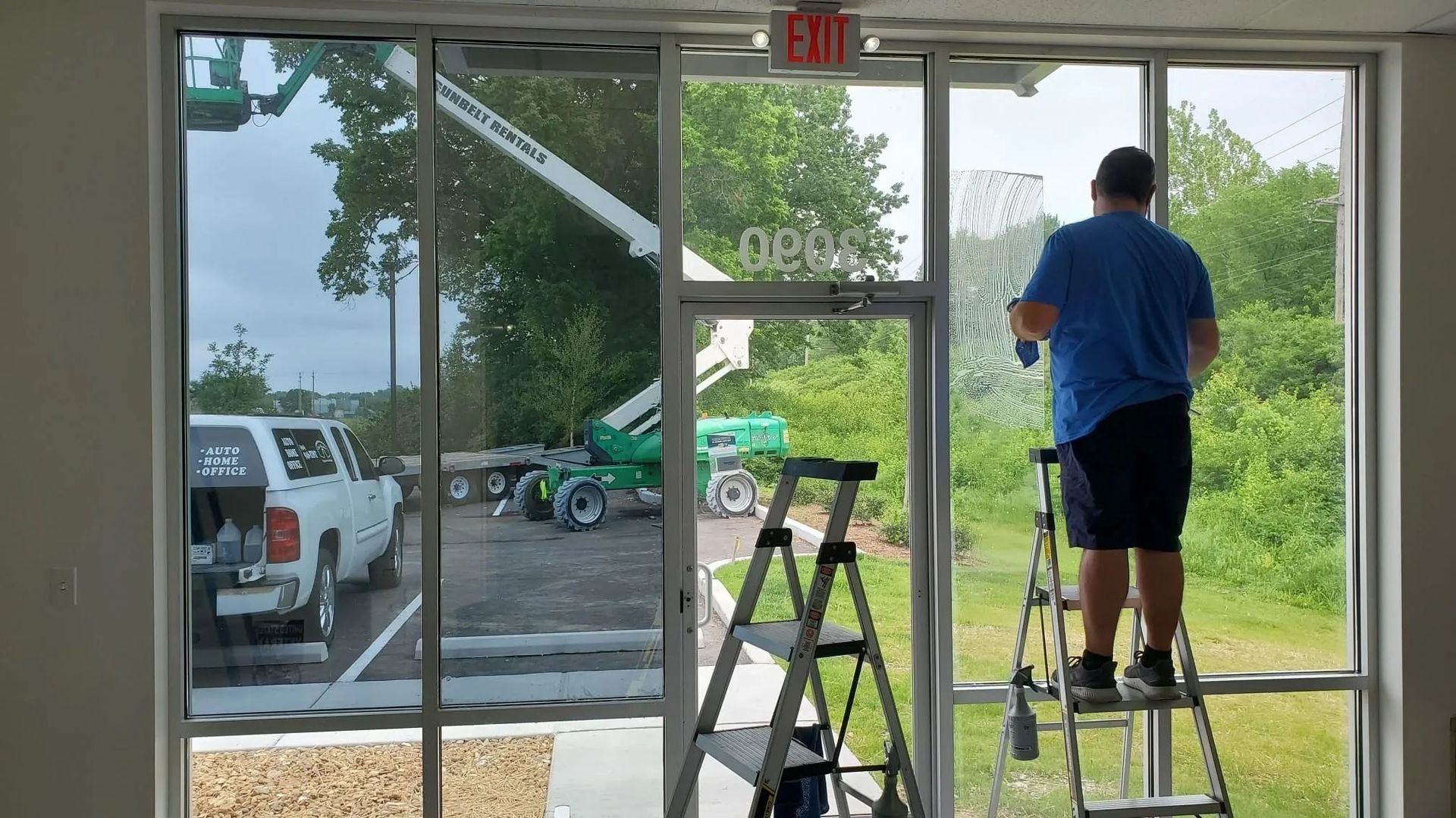 Worker cleaning glass storefront windows with a ladder inside a bright room