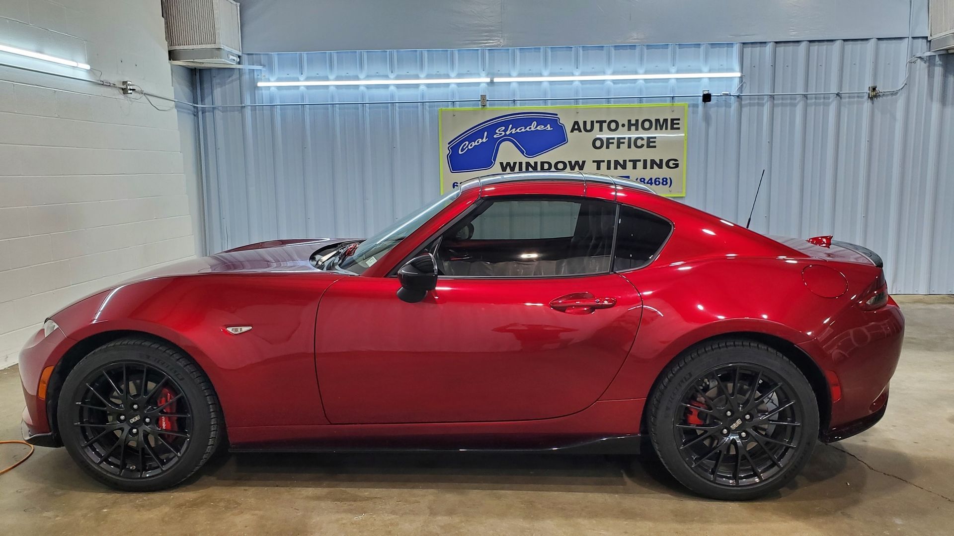 Red sports coupe in profile on a showroom floor with a blue sign behind it.