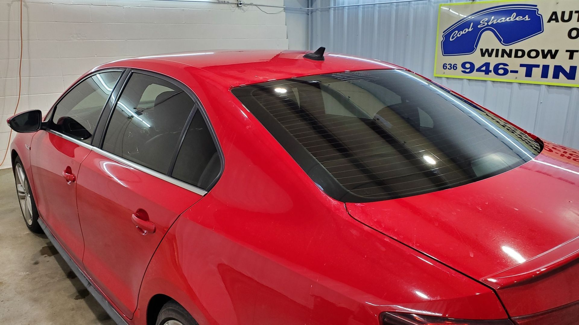Red sedan parked indoors in a garage, with a window tinting sign in the background