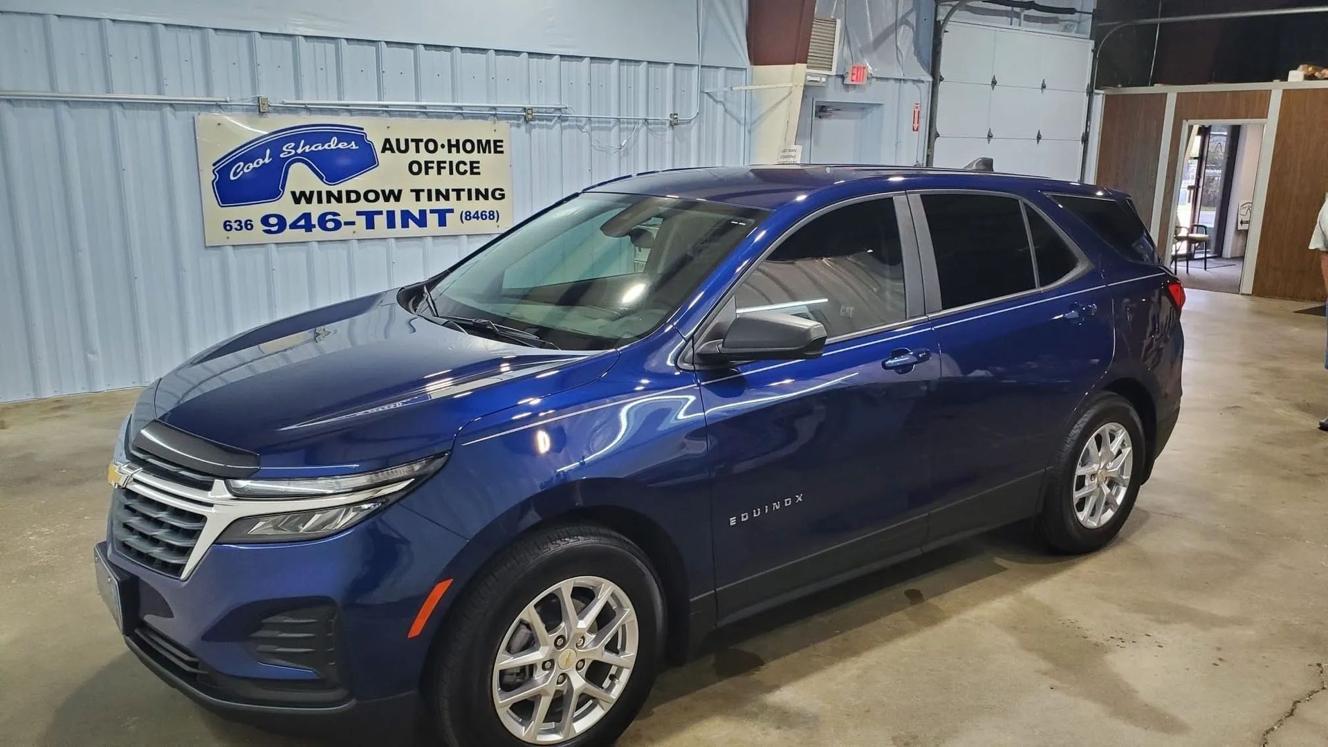 Blue SUV parked indoors at an auto tint shop with a sign in the background