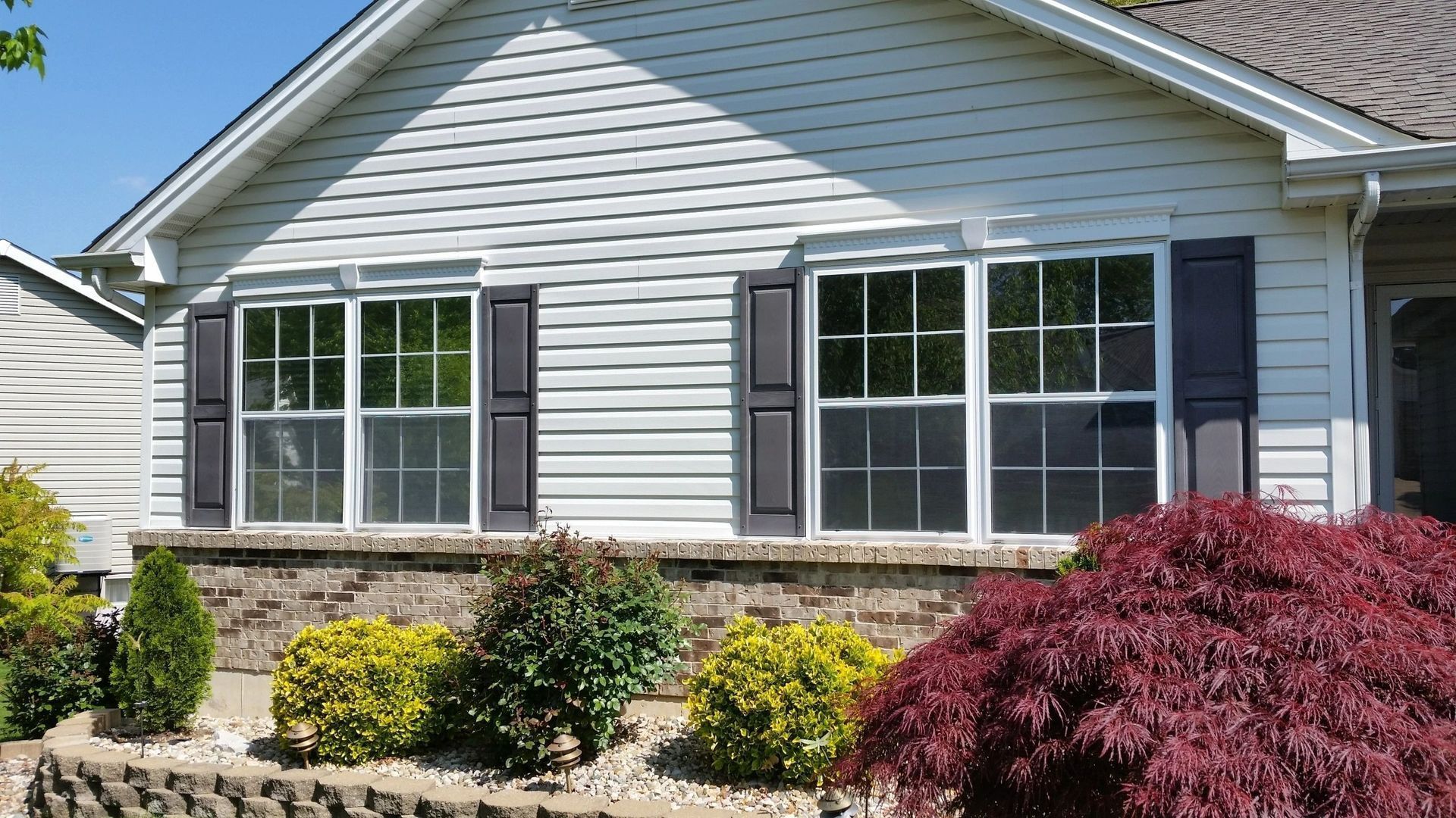 Suburban house exterior with gray siding, white trim, stone facade, and colorful front shrubs