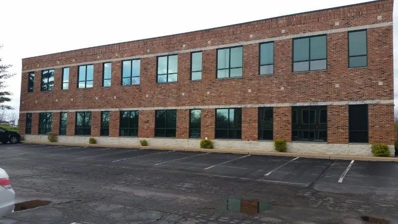 Two-story brick office building with many windows and an empty parking lot on an overcast day