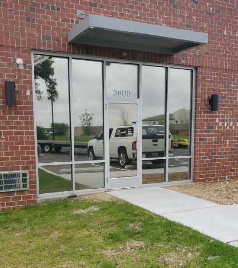 Brick building entrance with glass doors, black wall lights, and a concrete walkway