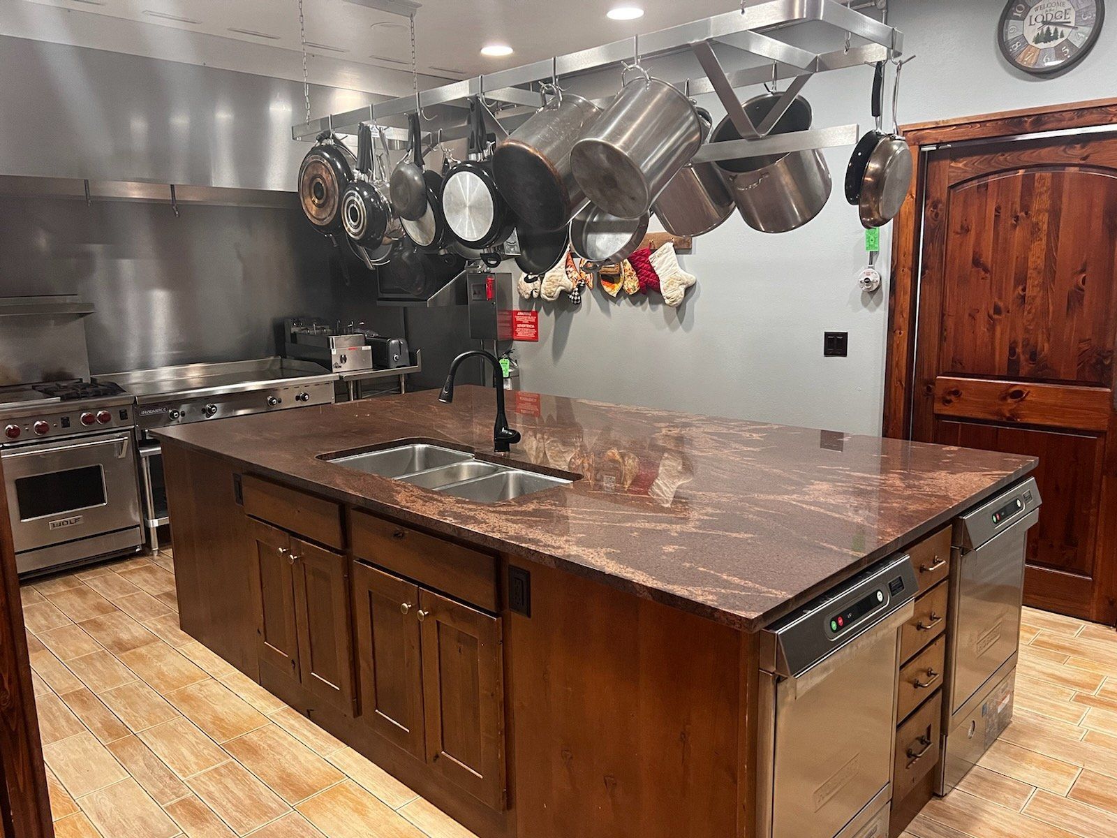 A kitchen with a large island , stainless steel appliances , pots and pans hanging from the ceiling.