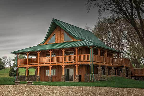 A large log cabin with a green roof and a large porch.