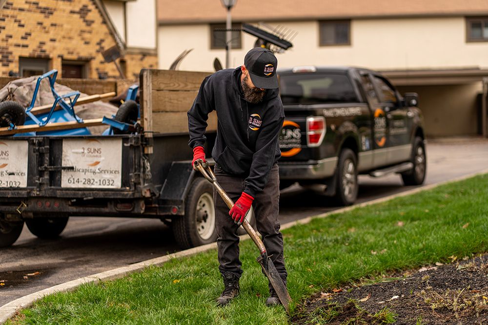 Man with shovel edging grass near a black truck and trailer; residential setting.