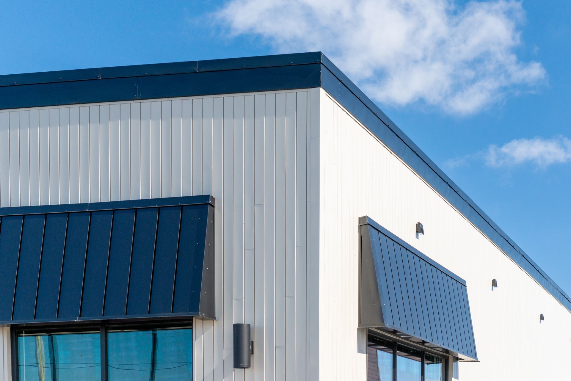 Le coin supérieur d'un bâtiment industriel blanc, orné d'auvents métalliques bleus et de garnitures bleues assorties, se détache sur un ciel bleu.