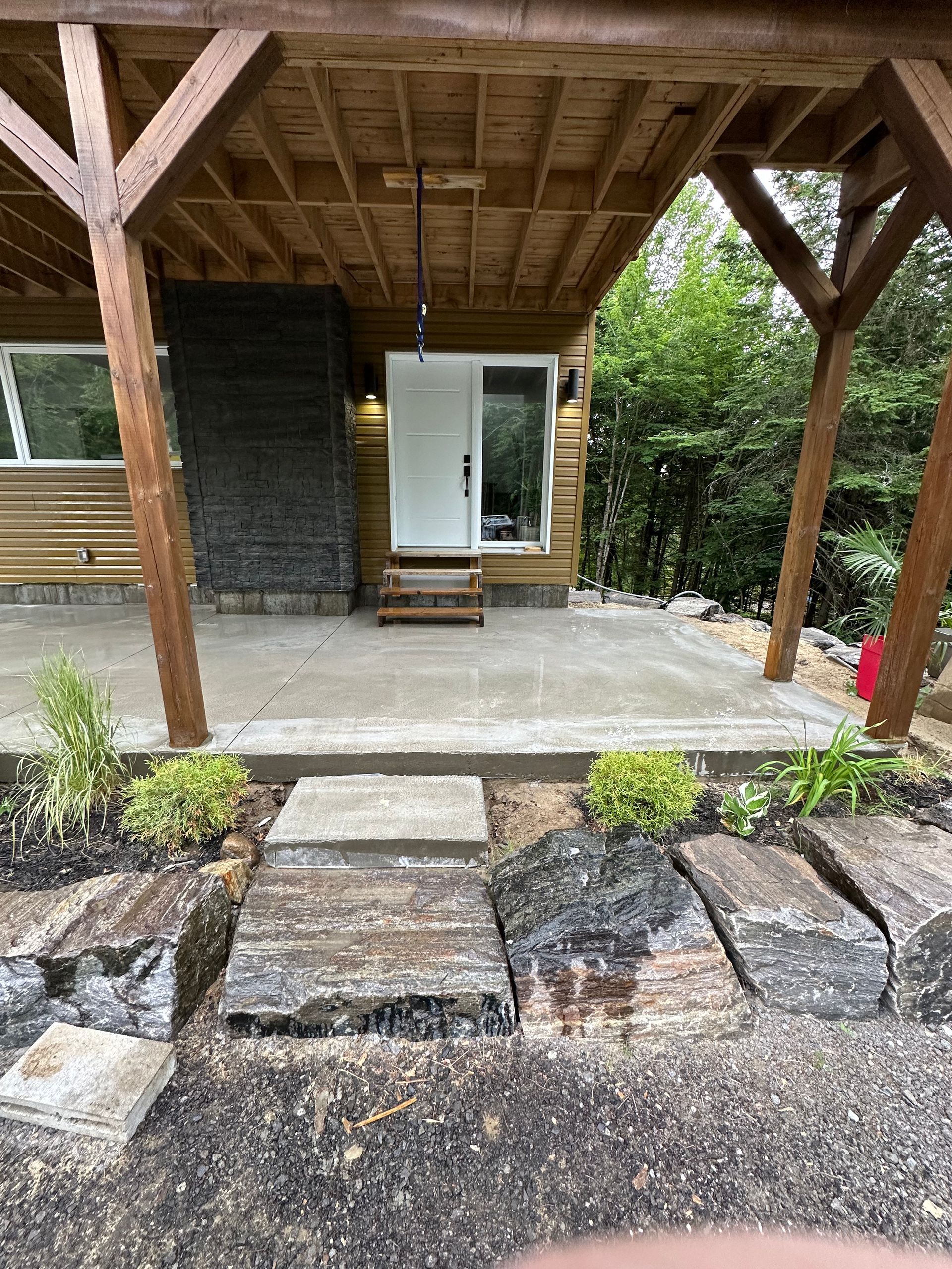 Une terrasse avec une porte blanche et des marches en pierre, encadrée par des poutres de soutien en bois sous un plafond en bois à aire ouverte.
