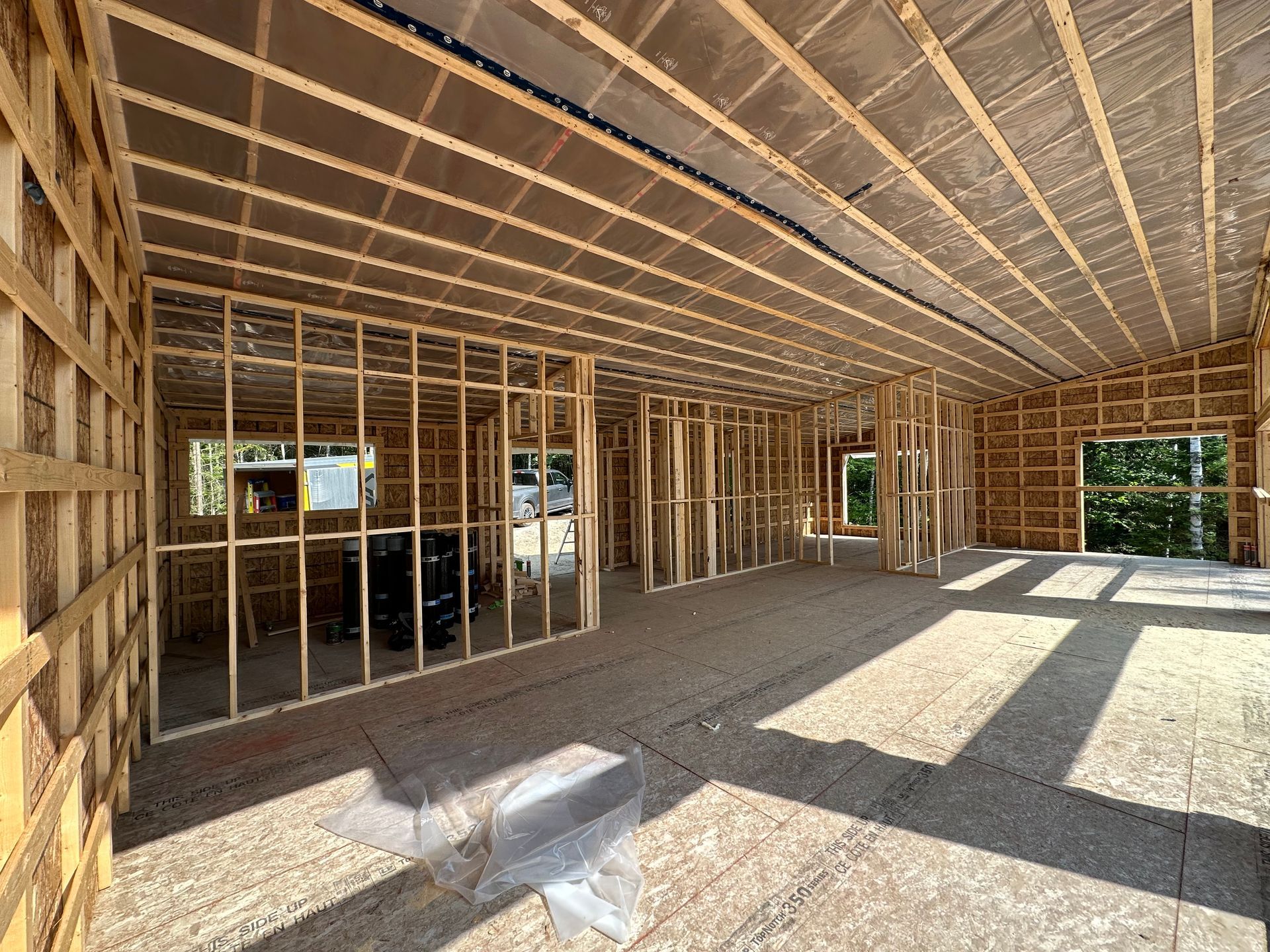 Vue intérieure d'un immeuble résidentiel en construction, avec des montants muraux en bois apparents et un sous-plancher en contreplaqué.