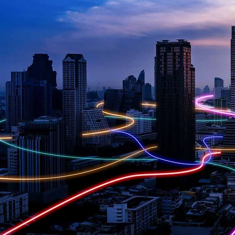 HIgh-rise city at dawn with coloured neon lines snaking around the buildings
