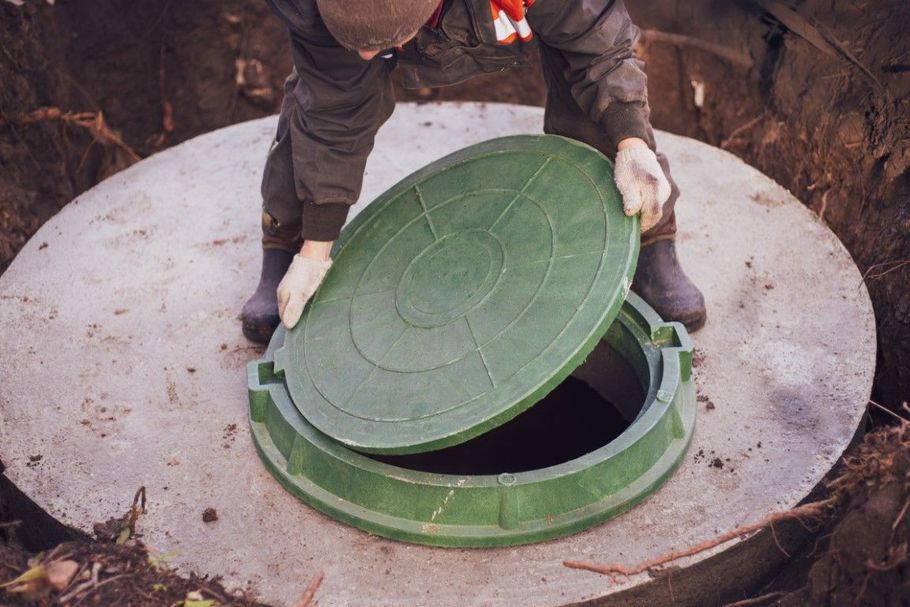 Person lifting a green manhole cover on a concrete utility access point