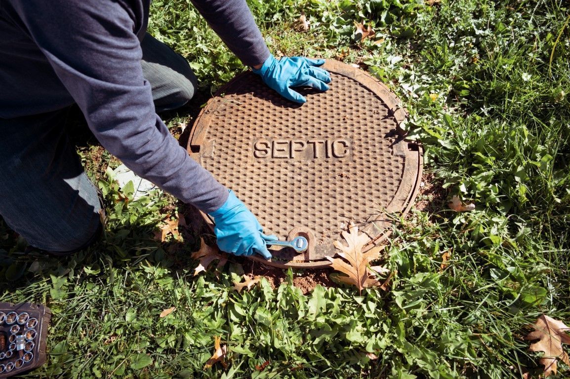 Worker in blue gloves opening a round SEPTIC manhole cover in grassy ground
